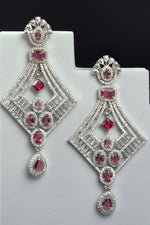Load image into Gallery viewer, Pair of diamond-shaped earrings with red gemstones on a white stand against a black background