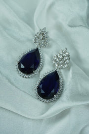 Navy blue teardrop earrings with silver accents on a white fabric background