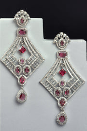 Pair of diamond-shaped earrings with red gemstones on a white stand against a black background
